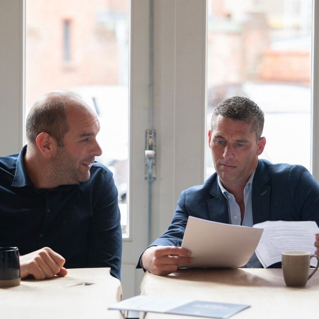 Twee experts van Schade Experts bespreken samen een schaderapport aan tafel